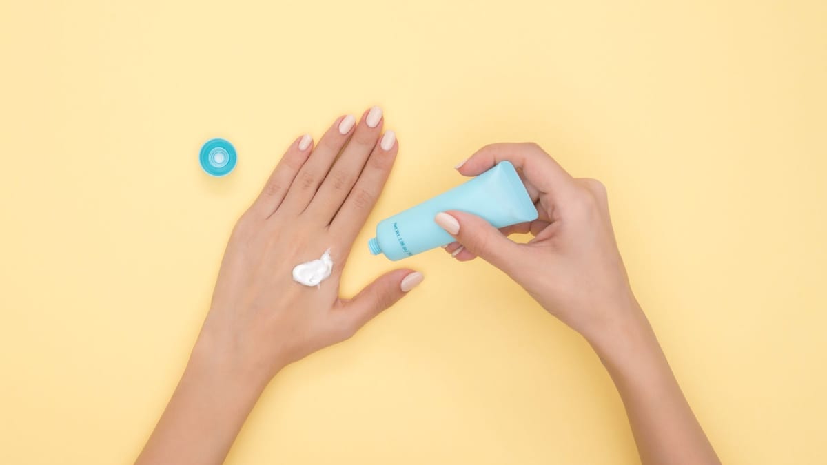 Hands squeezing a tube of moisturizer onto the back of one hand