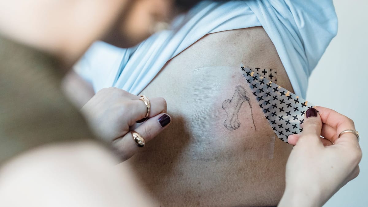 A clear film being peeled away from a small tattoo on the skin