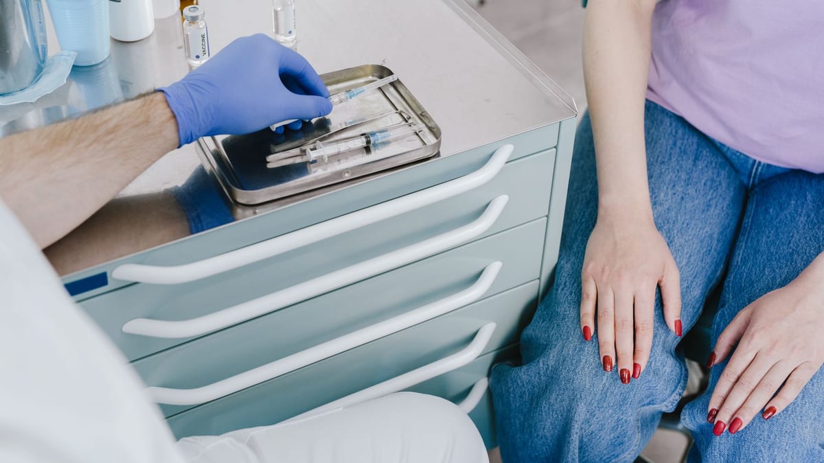 A syringe on a cosmetic clinic tray beside gloved hands