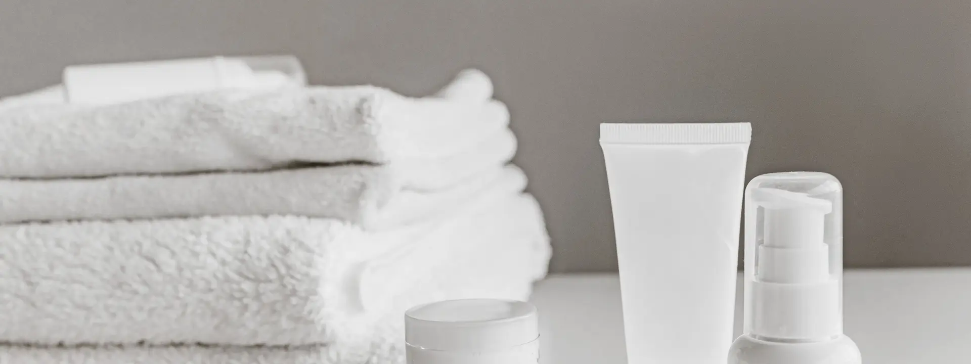 Plain white skincare bottles beside folded white towels